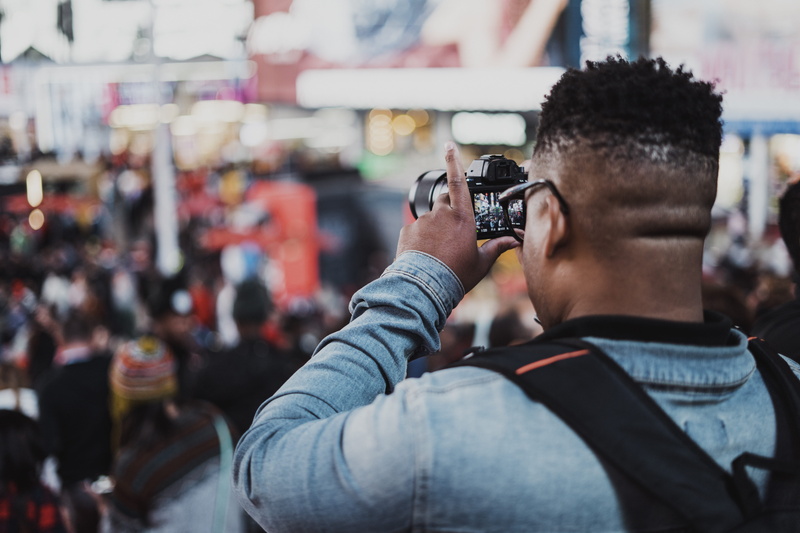 crowd, man, backpack, digital camera, black hair, selective focus, capturing, portrait, fashion, modern, city, holding, urban, using, outdoors, incidental people