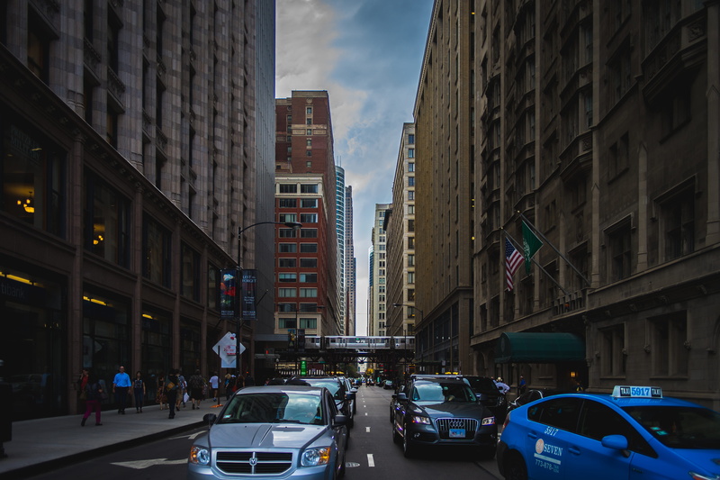 building, vehicles, street, rise, motor vehicle, built structure, lights, cityscape, blue, across, skyscraper, American flag, downtown, building exterior