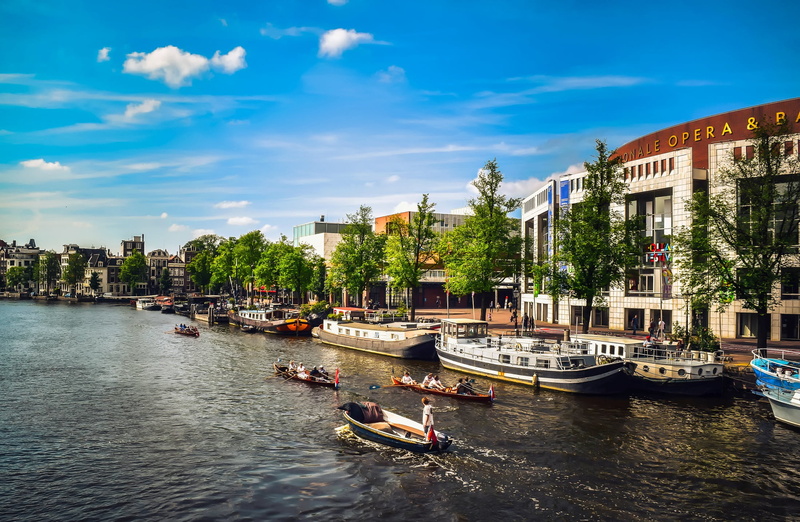 clouds, building exterior, building, built structure, tree, near, river, water, tourism, cloud - sky, travel, amsterdam, plant, blue, sky, mode of transportation