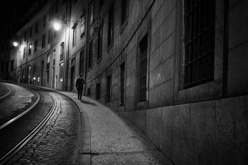 outdoors, illuminated, photo, rear view, track, 2K, real people, grayscale, beside, direction, men, building, building exterior, alley, road, night, built structure
