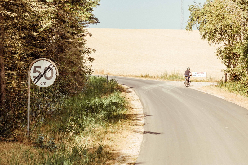 bicycle, vegetation, land vehicle, one person, summer, speed, road marking, human, direction, clock tower, gravel, road, grass, road sign, transportation