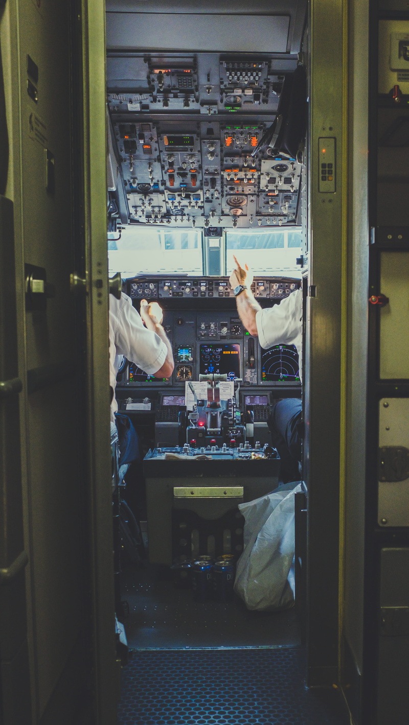 pilot, pointing, indoors, lifestyles, occupation, door, controls, seat, aircraft, real people, illuminated, mode of transportation, open, sitting, vehicle interior