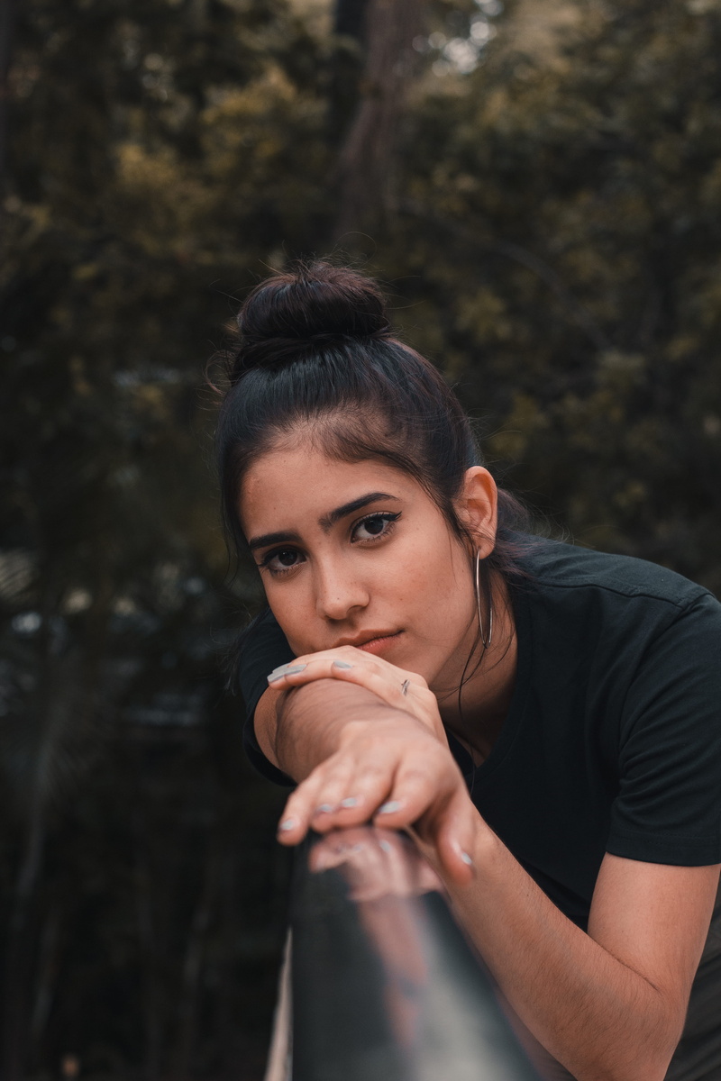 portrait, looking at camera, focus on foreground, 5K, casual clothing, young women, young adult, lifestyles, railings, black, chrome, hair, tree, arm