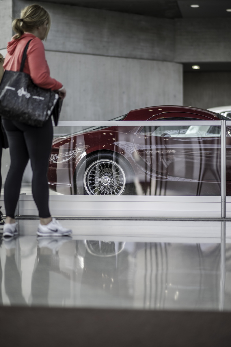 5K, mode of transportation, glass - material, wearing, car, red, rear view, standing, day, casual clothing, daytime, stance, glass, indoors, pants, woman