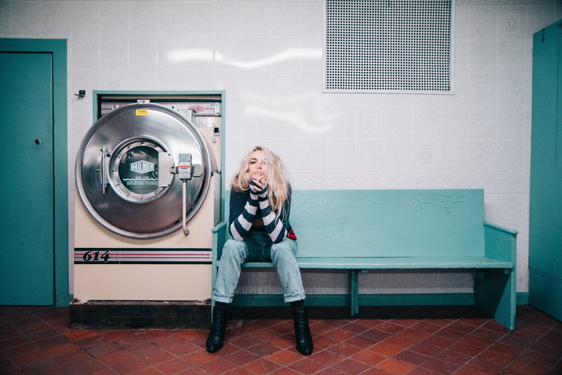 sitting, blonde, machinery, machine, waiting, sit, casual clothing, emotion, appliance, laundry, teal, people, adult, only women, woman, denim, indoors