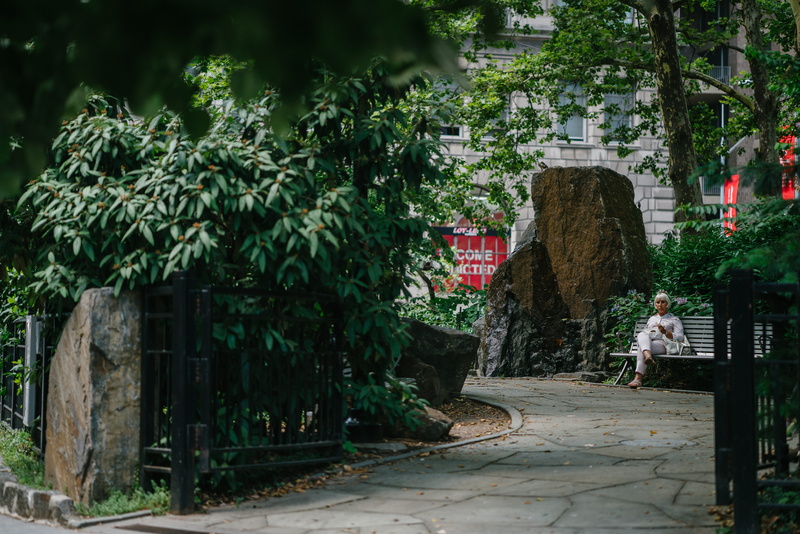building, outdoors, women, gate, sitting, plant, 8K, building exterior, stone pavement, garden, adult, bench, built structure, green color, footpath, full length