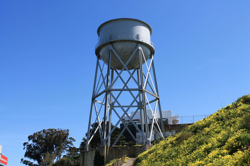industry, alcatraz, plant, america, tree, outdoors, water conservation, blue, sky, city, sunlight, landmark, storage tank, low angle view, center, historic