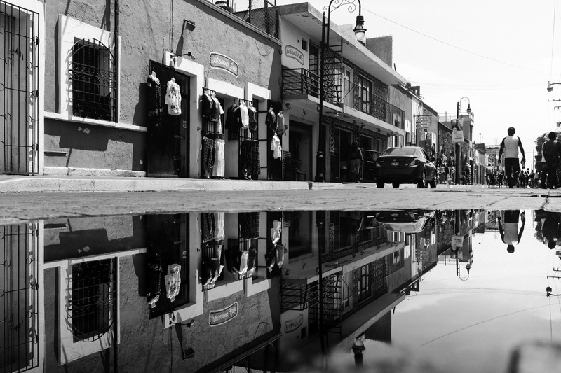 houses, grayscale, large group of people, people, black and white, reflection, sidewalk, car, built structure, water, transportation, day, puddle, group of people