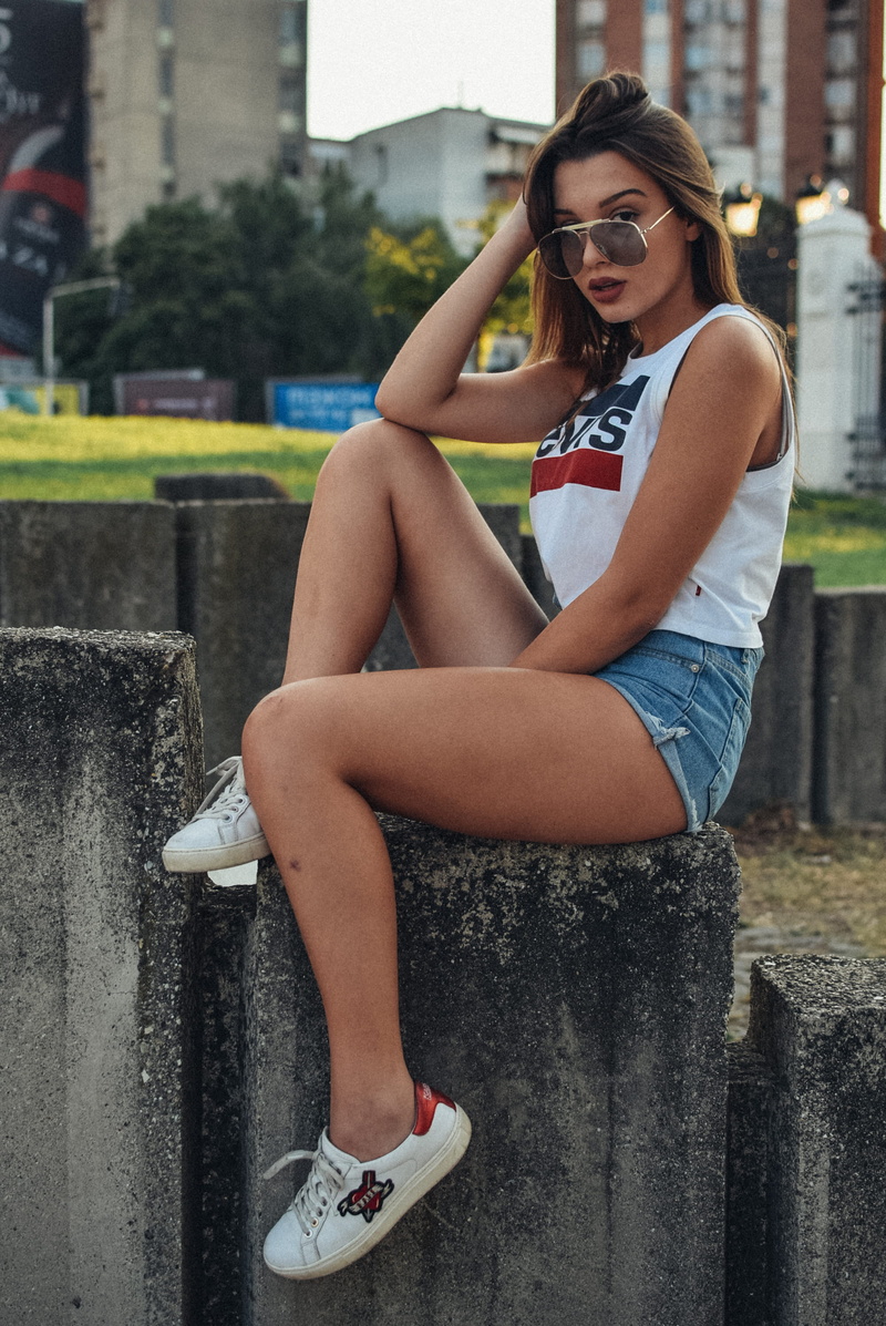 leisure activity, sitting, hairstyle, full length, outdoors, real people, wearing, shoe, lifestyles, young women, shorts, fashion, day, top, built structure