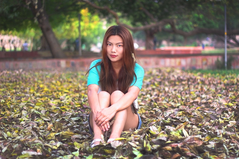 adults only, young adult, only women, front view, park, leaves, long hair, hairstyle, sitting on leaves, beautiful woman, brown hair, emotion, one person