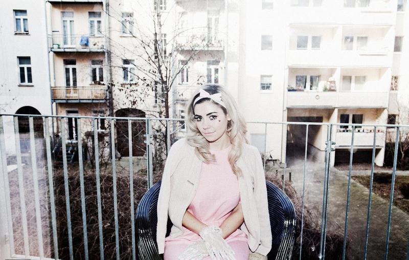 sitting, warm clothing, clothing, young adult, hair bows, architecture, building exterior, looking at camera, hairstyle, one person, standing, three quarter length
