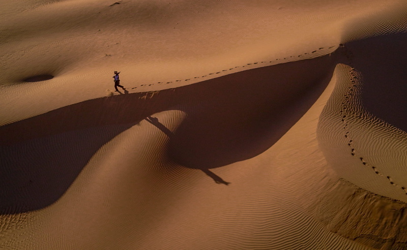 land, sand dune, sunset, dune, sunlight, non-urban scene, person, travel, scenic, high angle shot, adult, one person, desert, sand dunes, footprint, shadow
