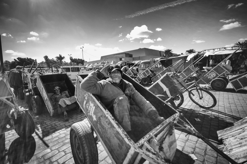 people, day, group of people, built structure, outdoors, working, wheel, cloud - sky, street, architecture, sleeping, land vehicle, incidental people, mode of transportation