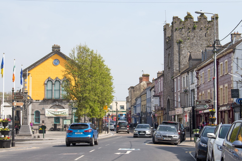 sign, road, mode of transportation, car, cashel, building exterior, town, buildings, license plate, asphalt, street, land vehicle, city street, sports car