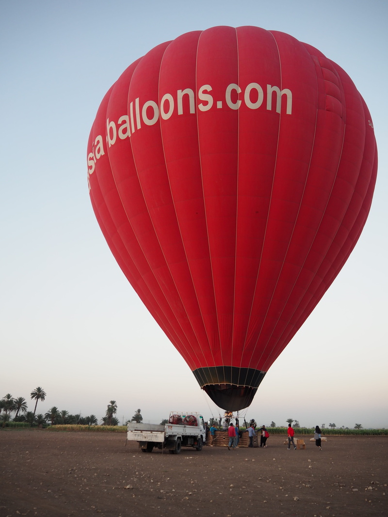 clear sky, land, text, desert, real people, adventure, transportation, day, nature, luxor, hot air balloon, sky, travel, air vehicle, people, red, incidental people