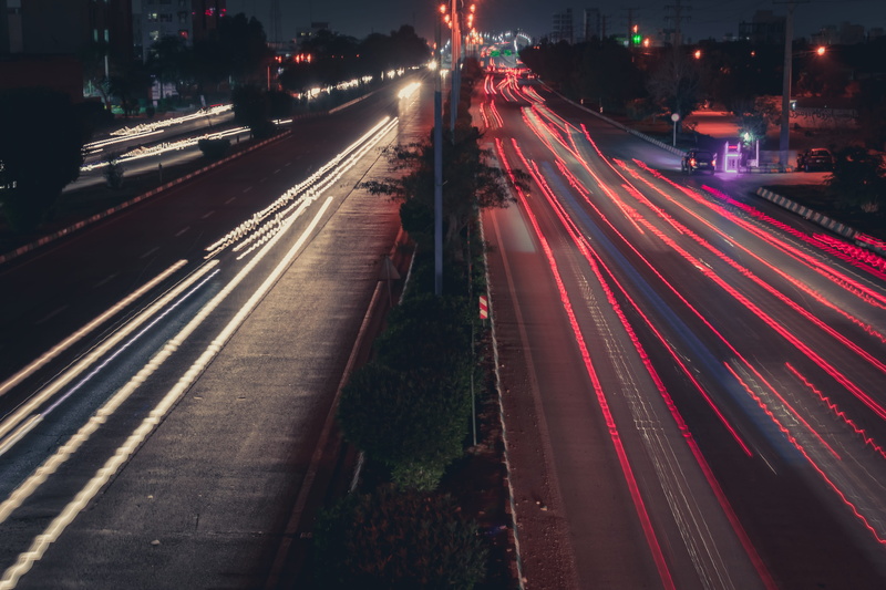 high angle view, flare, vehicle light, city life, traffic, street, mode of transportation, transportation, light trail, night, tarmac, light, human, highway