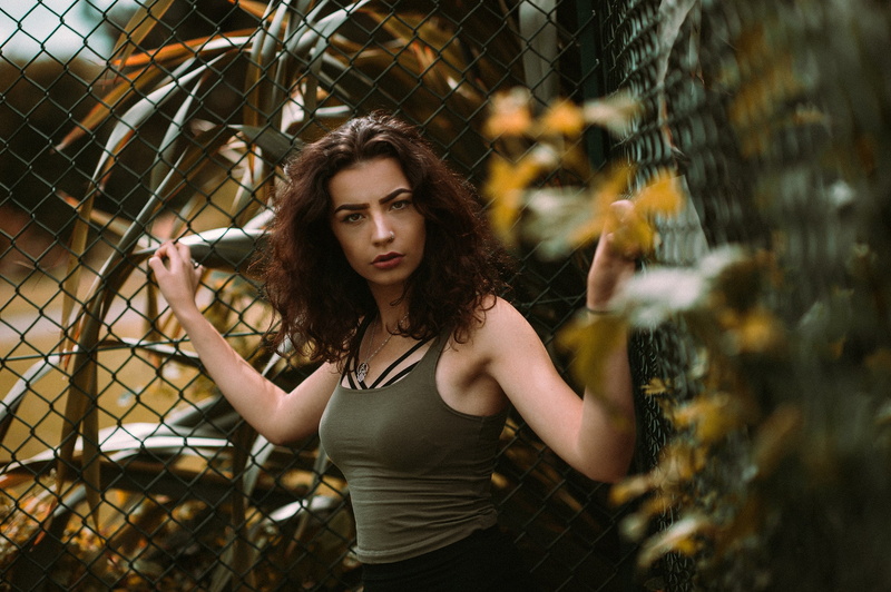 fence, hair, depth of field, brown hair, outdoors, adult, 1080P, fashion, women outdoors, hairstyle, necklace, looking at camera, chainlink fence, one person