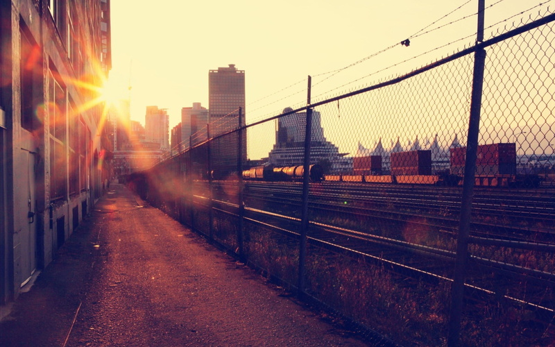 sky, railway, cityscape, no people, built structure, city, bridge, vehicle, nature, connection, sun, fence, building exterior, train, sunlight, outdoors