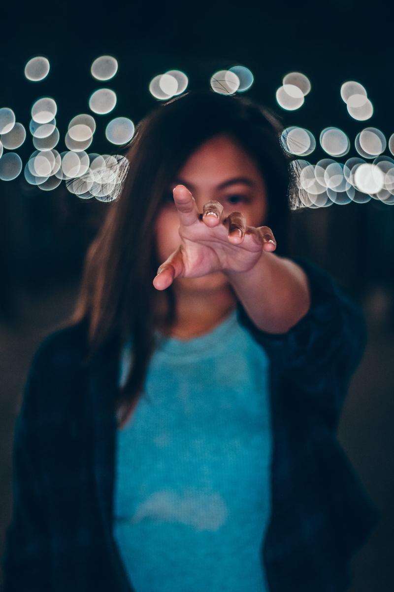 hand, finger, daisy, beautiful woman, money, daisies, bokeh, plant, focus on foreground, indoors, blossom, person, holding, light, looking at camera, casual clothing