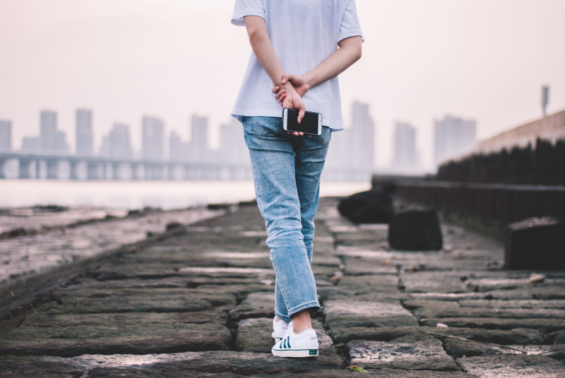 face, outdoors, 4K, sneaker, one person, sitting, phone, wearing, slate, nature, building exterior, day, lifestyles, sky, casual clothing, path, clothing