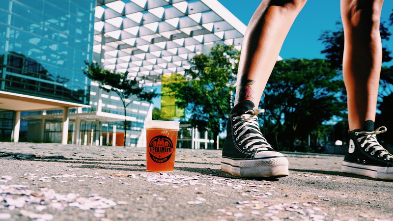 cup, person, outdoors, shoe, sunlight, human foot, building, glass, drink, city, footwear, architecture, running shoe, sneaker, top, patio, surface level