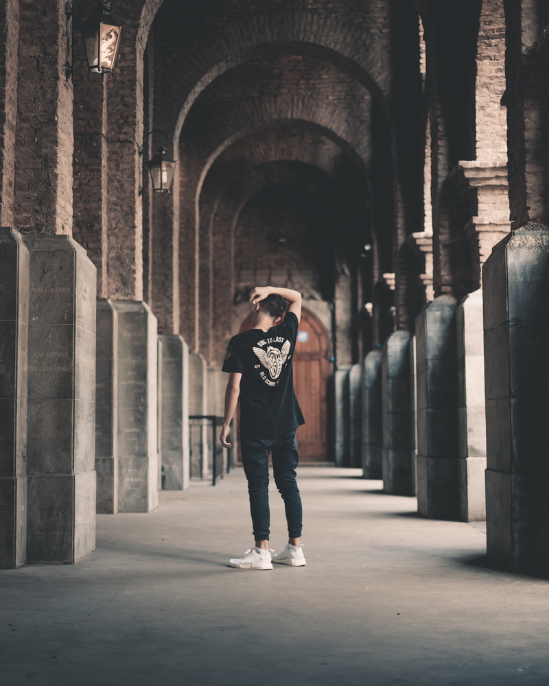 one person, black shirt, standing, concrete wall, clothing, footwear, real people, stand, hallway, back view, photoshoot, the past, front view, history