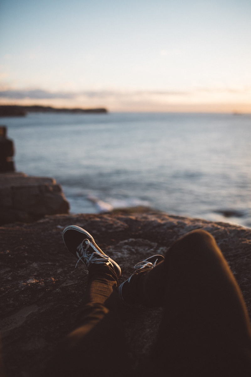 outdoors, shoe, solid, water, brown, nature, beach, wearing, tranquil scene, ocean, looking out, rest, sitting, low, person, sun, formation, rock - object