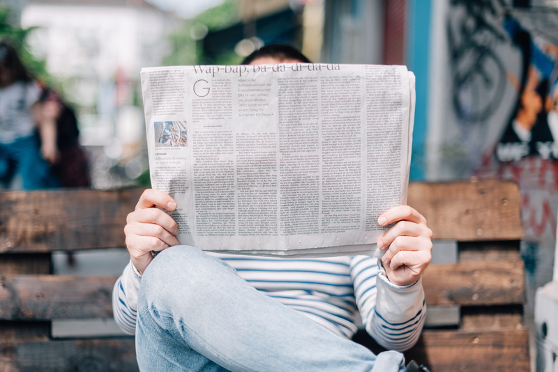 people, reading, sitting, bench, casual clothing, information medium, obscured face, paper, lifestyles, newspaper, book, one person, holding, activity