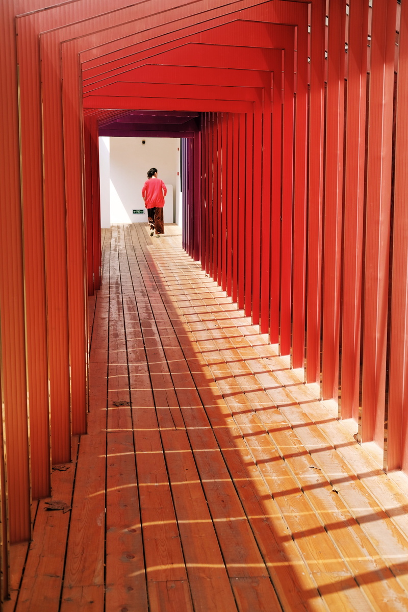 rear view, one person, in a row, wooden, diminishing perspective, 5K, day, person, human, orange color, walkway, woman, full length, floor, deck, red