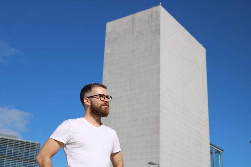 architecture, near, standing, sky, sunny, beard, male, one person, facial hair, adult, casual clothing, post, building, beside, young adult, 5K, stand