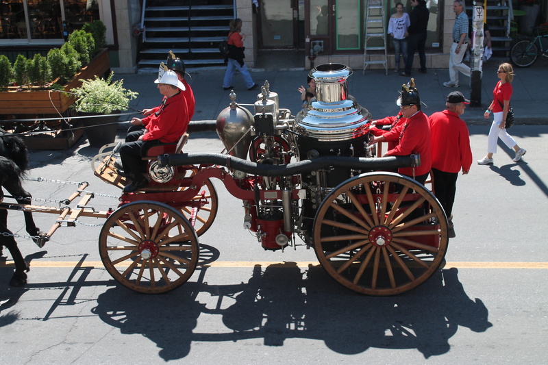 cartwheel, building exterior, medium group of people, sunlight, parade, Truck, bicycle, built structure, land vehicle, street, full length, costume, adult