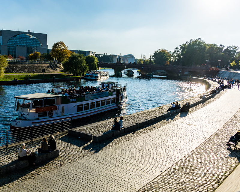 incidental people, tree, berlin, day, river, boats, water, built structure, passenger craft, travel, building exterior, mode of transportation, bridge