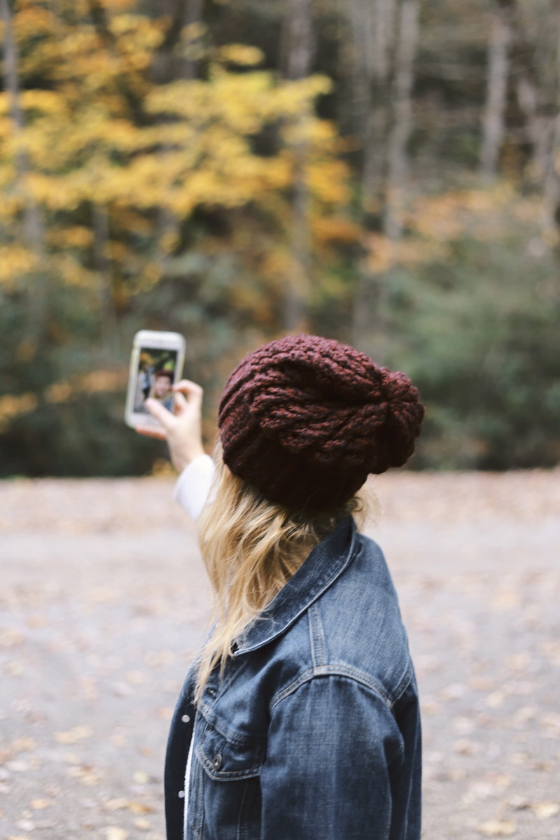 pants, apparel, mobile phone, woman, outdoors, cap, focus on foreground, beanie, real people, selfie, one person, hairstyle, clothing, photographing, female