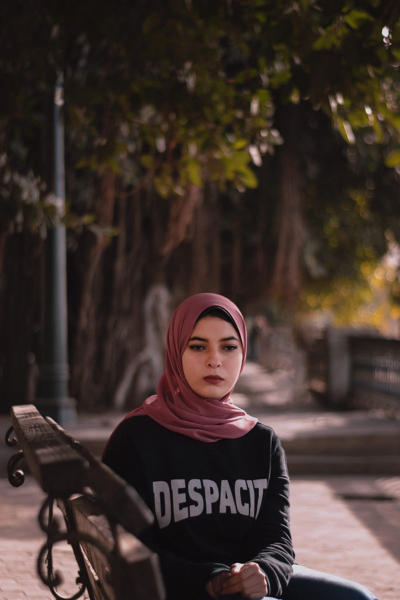 finger, weaponry, transportation, bench, adult, hat, outdoors, clothing, bike, sweater, real people, tree, looking at camera, one person, front view, focus on foreground