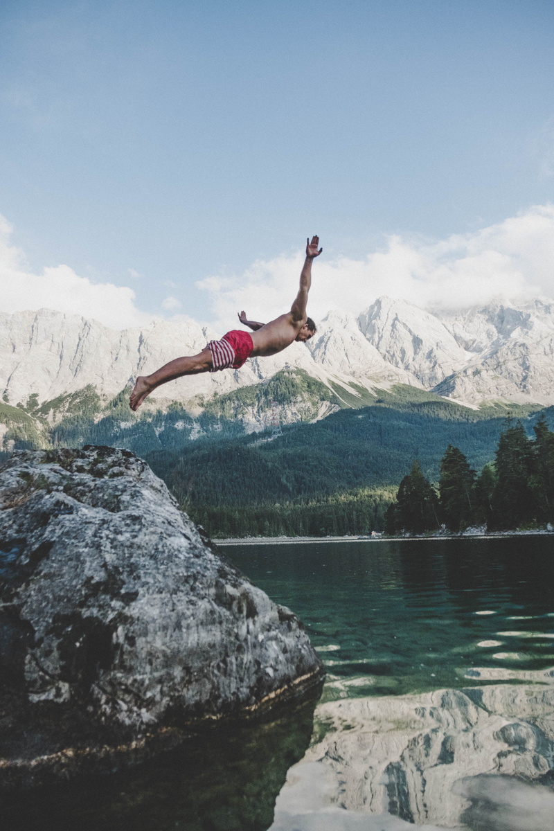 beauty in nature, short, wearing, water, human arm, one person, leisure activity, cold, arms raised, board, rock, action, daylight, sky, body part, rock - object