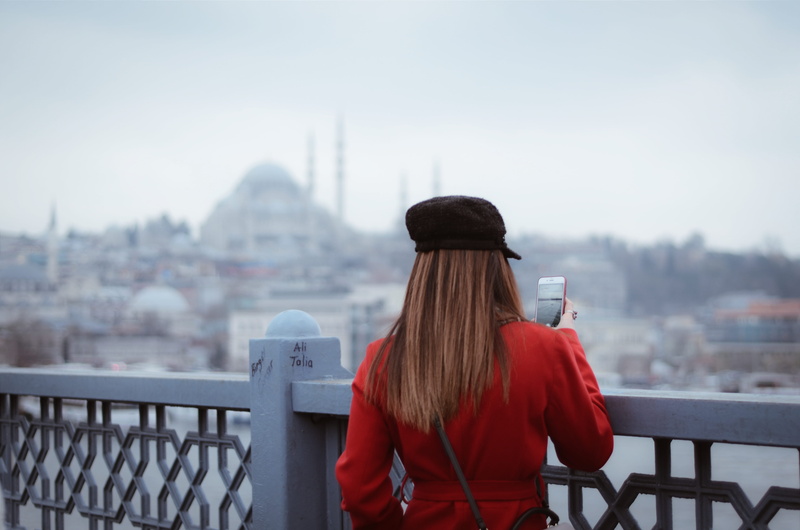 one person, back view, women, warm clothing, bridge railing, standing, adult, city, hair, blurred background, rails, tourist, building exterior, real people