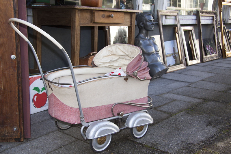 junk, mode of transportation, sculpture, day, frame, art and craft, bust, built structure, beside, wooden, land vehicle, old, door, sidewalk, baby carriage
