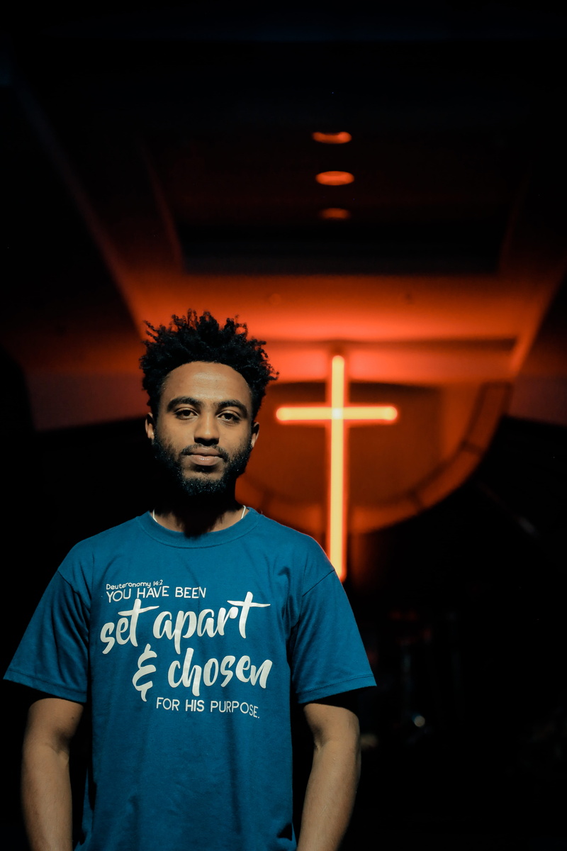 looking at camera, serious, human, t-shirt, religion, symbol, text, fashion, young adult, sleeve, person, male, communication, waist up, church, model