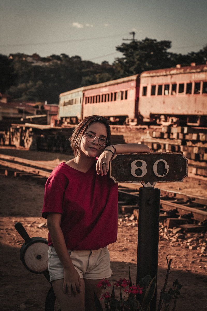 one person, text, built structure, pose, road, locomotive, railroad, wearing, signage, communication, western script, railroad tracks, railway line, photoshoot
