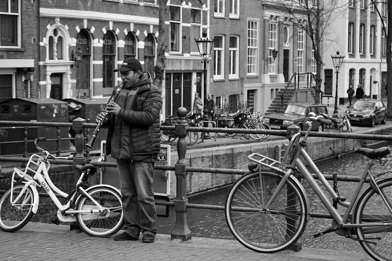standing, acoustic, bicycles, architecture, wind instrument, scene, street musicians, houses, bicycle, street music, bridge, street, day, one person, land vehicle