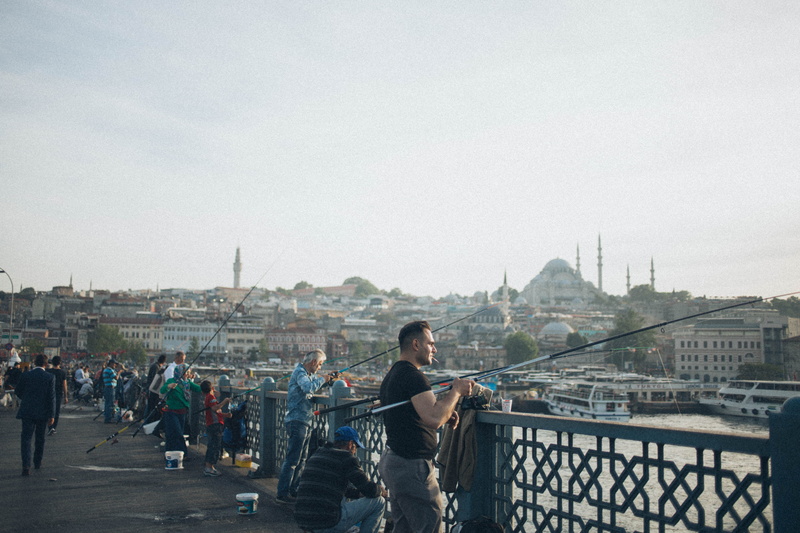 bridge - man made structure, men, city, railing, musical instrument, architecture, city life, water, bridge, building exterior, leisure activity, fishing