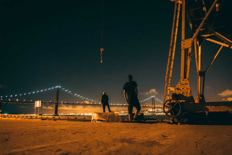 person, style, metal, fashion, city, outdoors, standing, men, light, built structure, sky, water, machinery, hook, bridge - man made structure, black, connection
