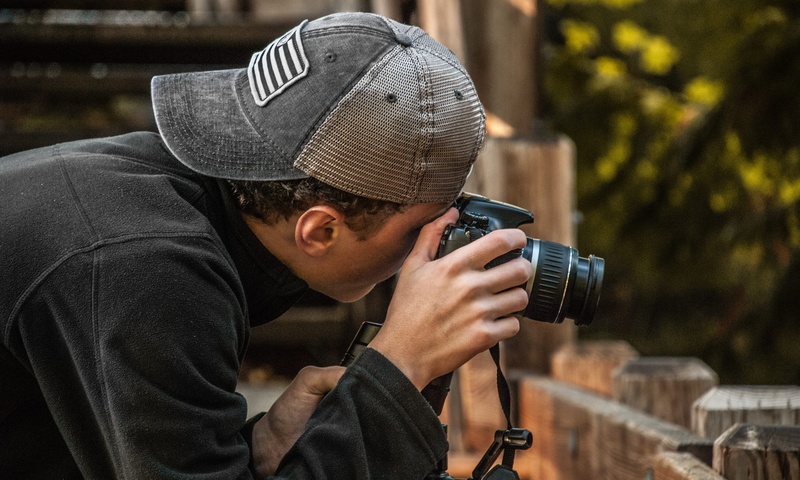 camera equipment, activity, cap, trees, camera, dslr, street, men, clothing, young adult, hat, casual, portrait, wear, field, male, depth of field, headshot
