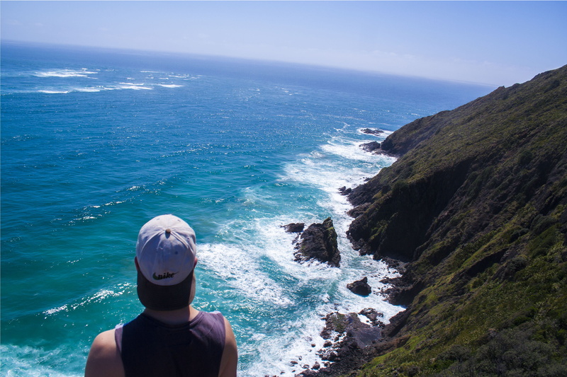 sky, nature, outdoors, blue, day, rocks, rock - object, looking at view, one person, beauty in nature, sea, leisure activity, rear view, land, cape reinga