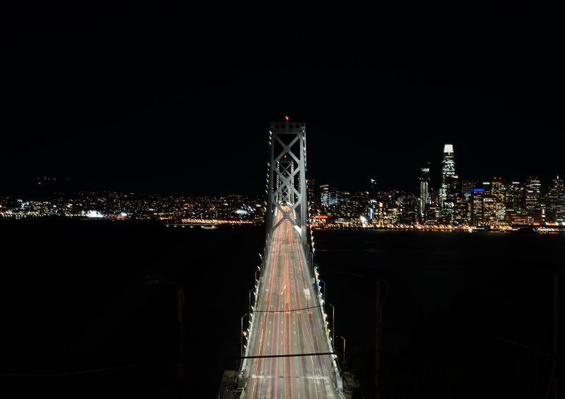 bridge, city, bay bridge, boardwalk, banister, tower, outdoors, building exterior, travel destinations, metropolis, building, motion, gray, skyscraper