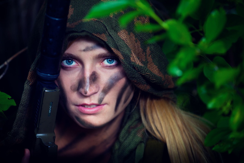 hair, looking at camera, real people, 1080P, hairstyle, blonde, girls with guns, one person, hood - clothing, portrait, clothing, model, weapon, headshot