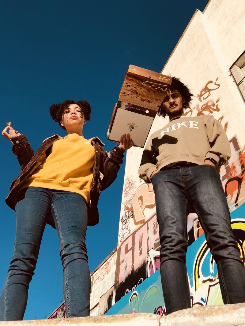 casual clothing, next, sunlight, persons, woman, built structure, pizza, young adult, jacket, clear sky, low angle view, architecture, black, wearing, building exterior