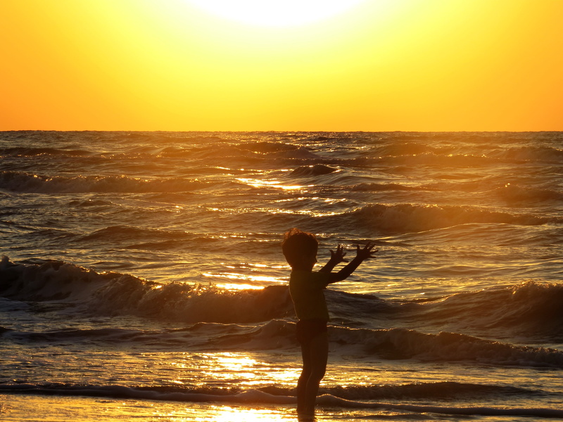 shore, water, beauty in nature, sky, horizon, orange color, horizon over water, child, ocean, real people, boy, arms raised, human arm, sunrise, leisure activity