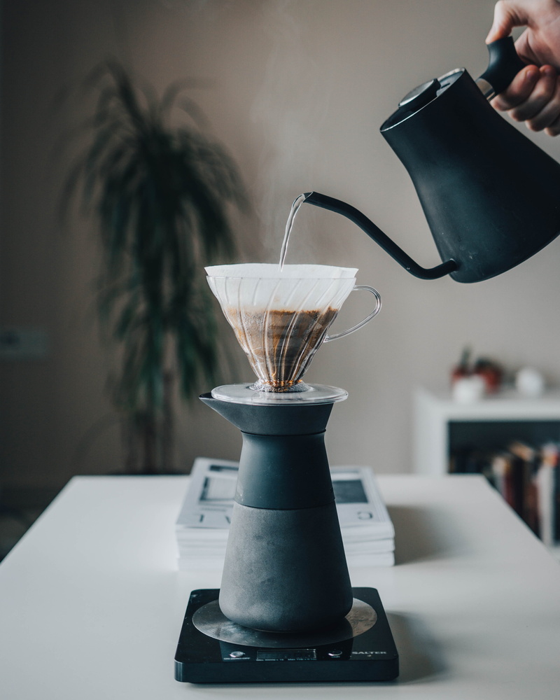 real people, table, mug, water, coffee, person, indoors, hand, pour, pouring, drink, focus on foreground, preparation, coffee maker, food and drink, cup