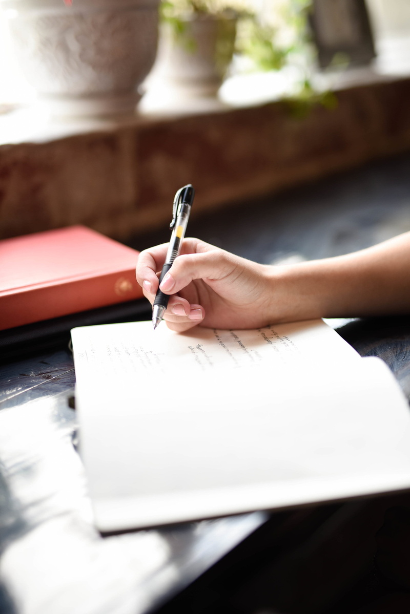 table, lifestyles, indoors, publication, hand, note, writing instrument, unrecognizable person, human limb, one person, holding, paper, creativity, selective focus